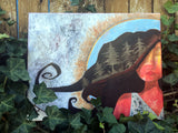 feminine artwork depicting a woman with a silhouette of a forest in her hair and organic, earth tone texture and markings behind her.  the painting is sitting in some vines along a fence.