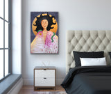 A mixed media painting of a woman with a snake draped over her shoulders is hanging on a wall over a bedside table.  On the left side of the frame is a window with sunlight coming in, and on the right is a bed with black bedding and a cushioned beige headboard.