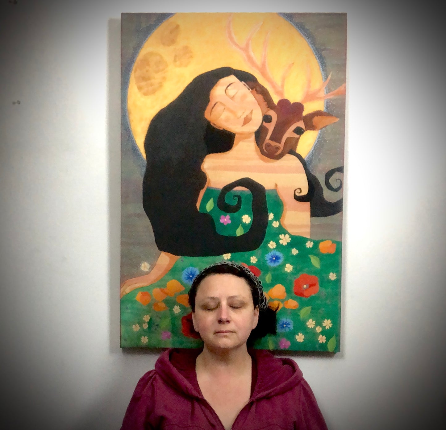 Portland artist Lea K. Tawd meditating in front of her painting "Guided."  The painting shows a beautiful woman with her eyes closed and a stag resting his head on her shoulder.