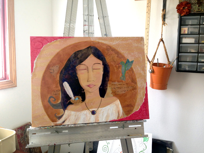 mixed media painting of a woman with a hummingbird and a bird's nest.  The painting is on an easel in artist Lea K. Tawd's studio