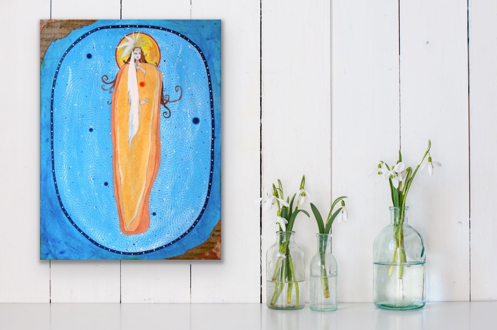 orange and blue mixed media feminine painting on a rustic white wall with 3 glass vases filled with flowers next to it.