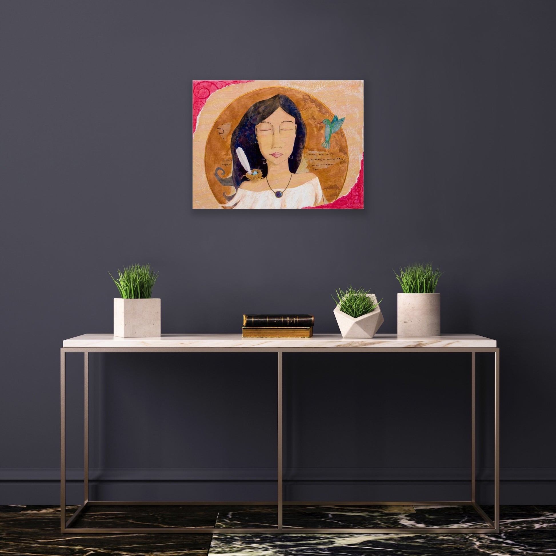 spiritual feminine artwork hanging on a dark grey wall above a white table with geometric concrete planters on it.