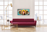 spiritual feminine artwork hanging on the wall between two large windows in a room with a burgundy sofa and golden tables and lamps