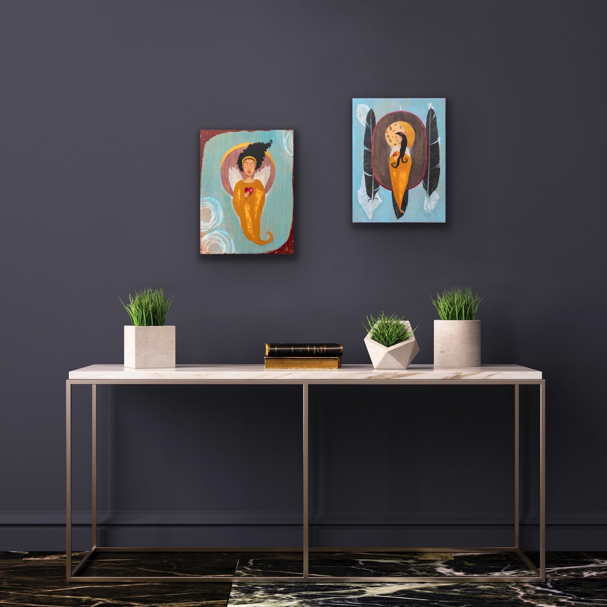 Two small paintings of female figures with hearts in their hands.  The paintings are hanging on a gray wall above a white table with cement planters and books.
