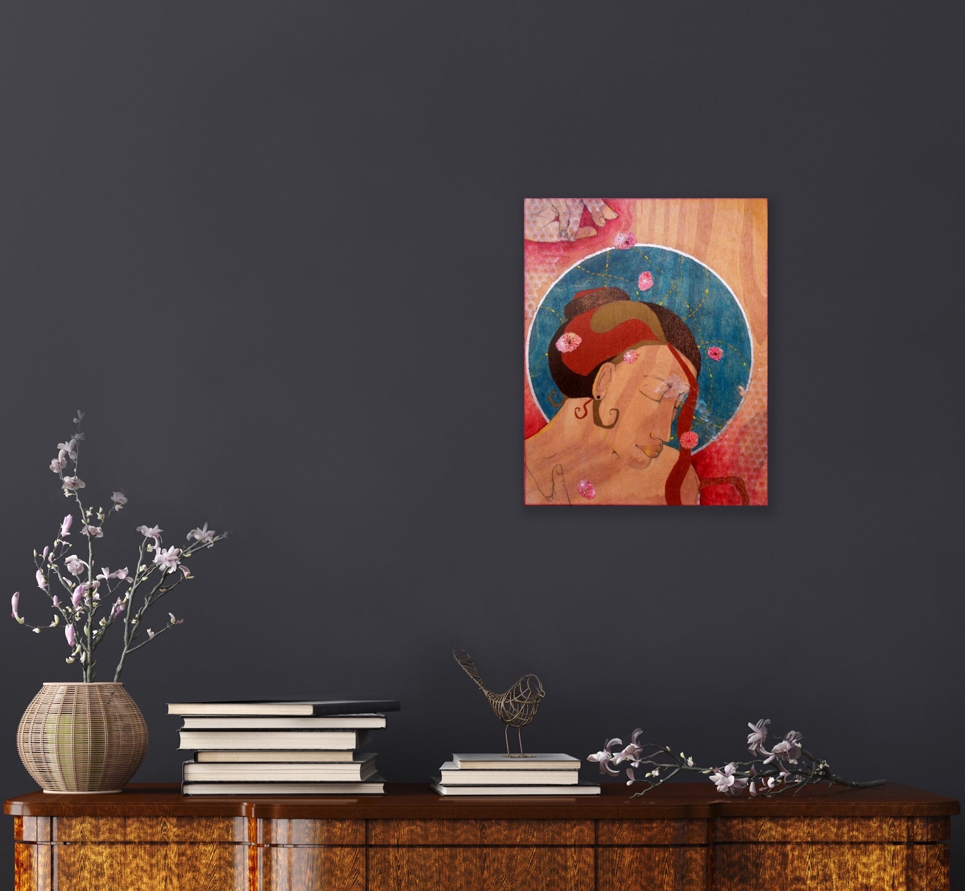 warm toned feminine painting on wood hanging on a dark grey wall above a golden wood table covered in books and decorative flowers and bird