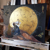 golden moon constellation painting with woman kneeling at a fire. Painting is on an easel and shown at an angle in order to show the gold of the moon.